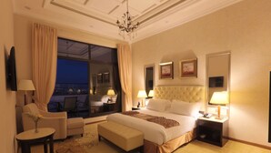 Habitación de hotel con una cama grande, una zona de estar con una silla y una mesa, un escritorio pequeño y vistas por una ventana amplia.