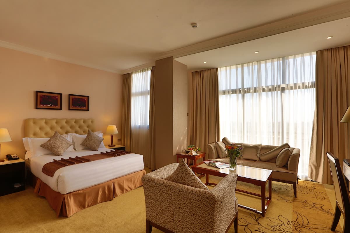 A hotel room with a large bed, a sofa, a coffee table, and a desk.