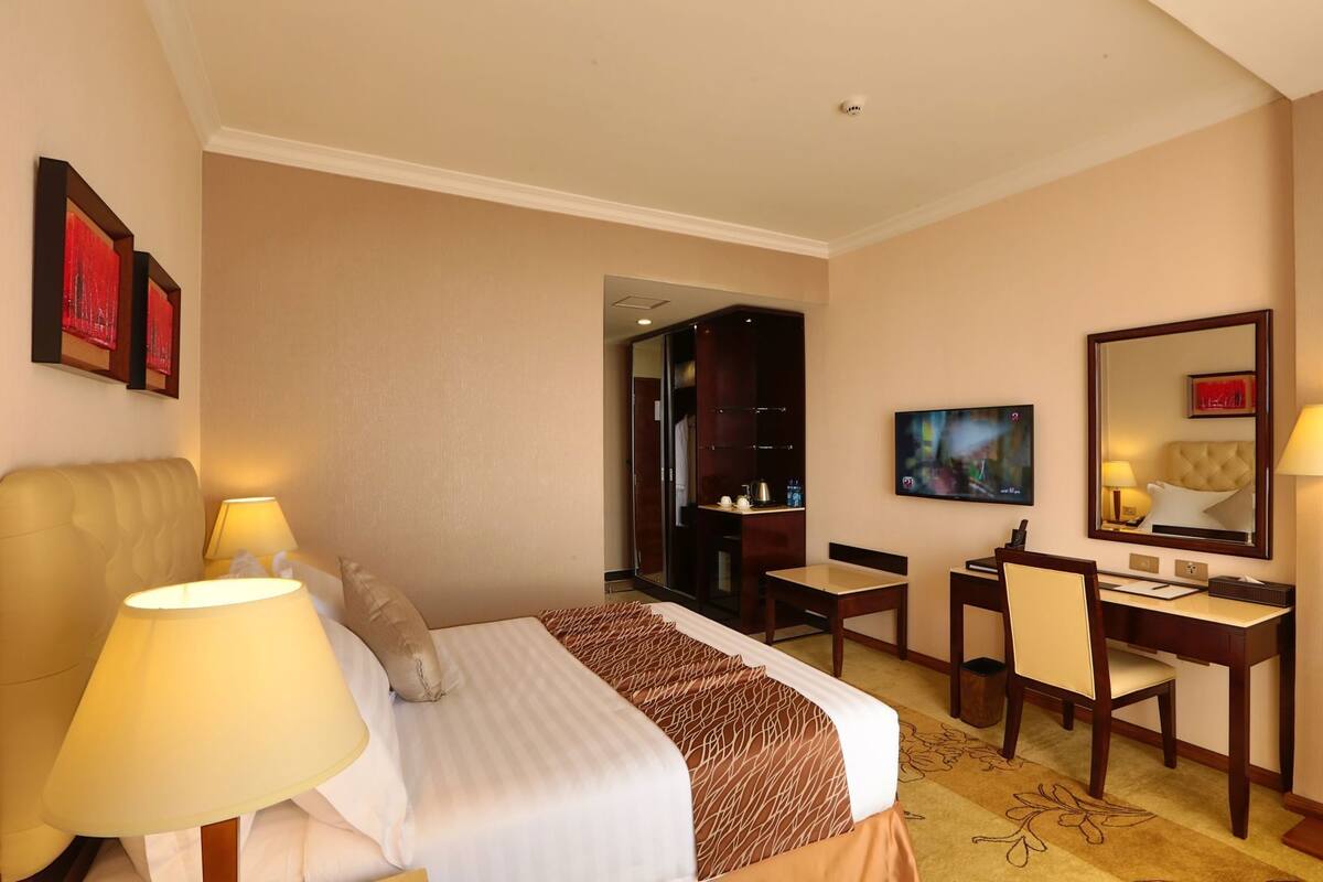 A hotel room with a bed, desk, chairs, a TV, and a mirror.