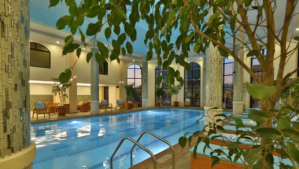 Una piscina interior con agua cristalina, rodeada de sillones de descanso y un ventanal grande.