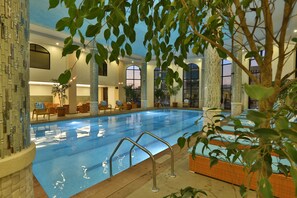 An indoor swimming pool with clear water, surrounded by lounge chairs and a large window. - Getfam Hotel (Addis Ababa)