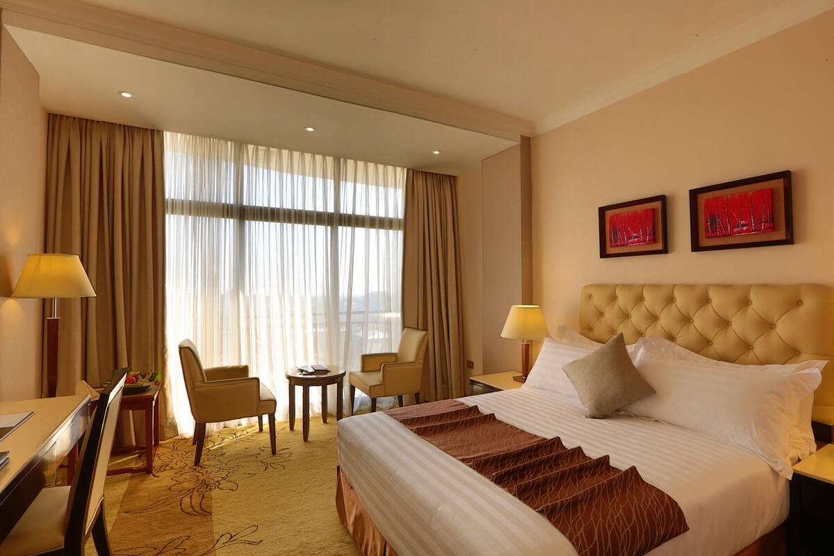 A hotel room with a large bed, two chairs, a small table, and a desk. There are two framed pictures on the wall.