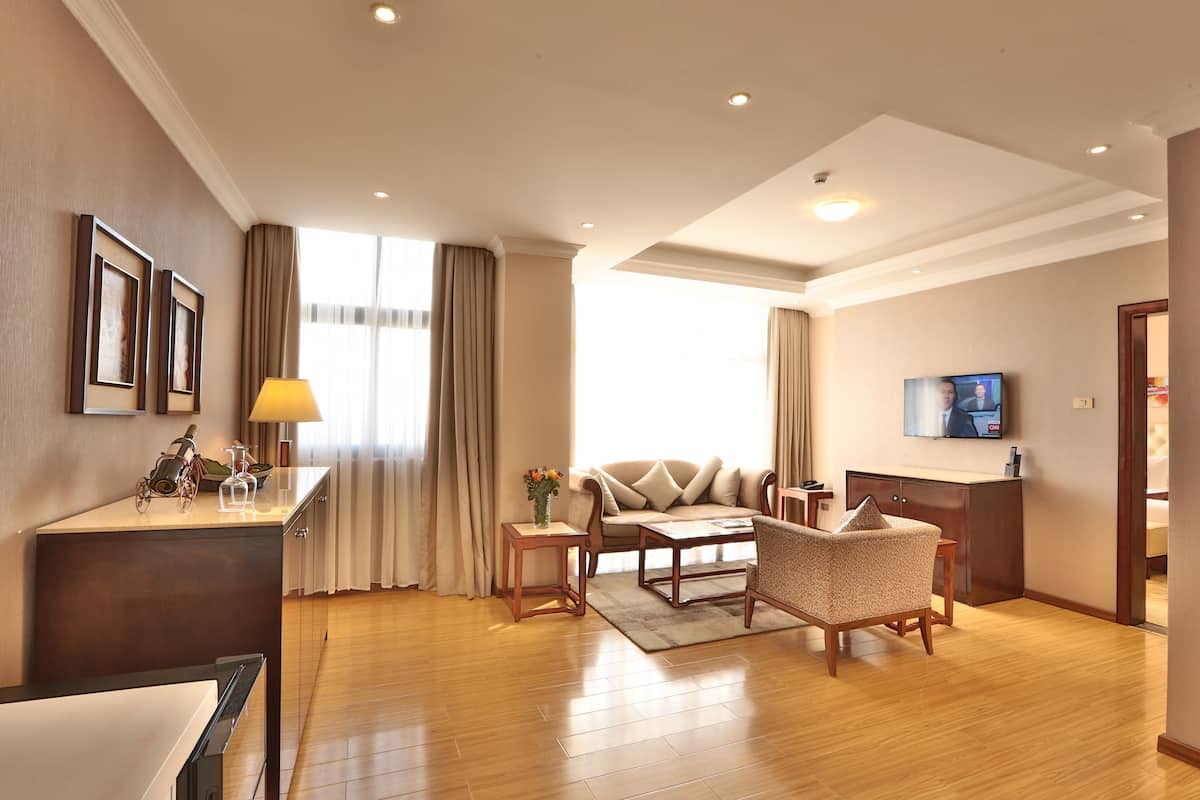 A modern hotel room with a sofa, armchair, and a small desk with a lamp.