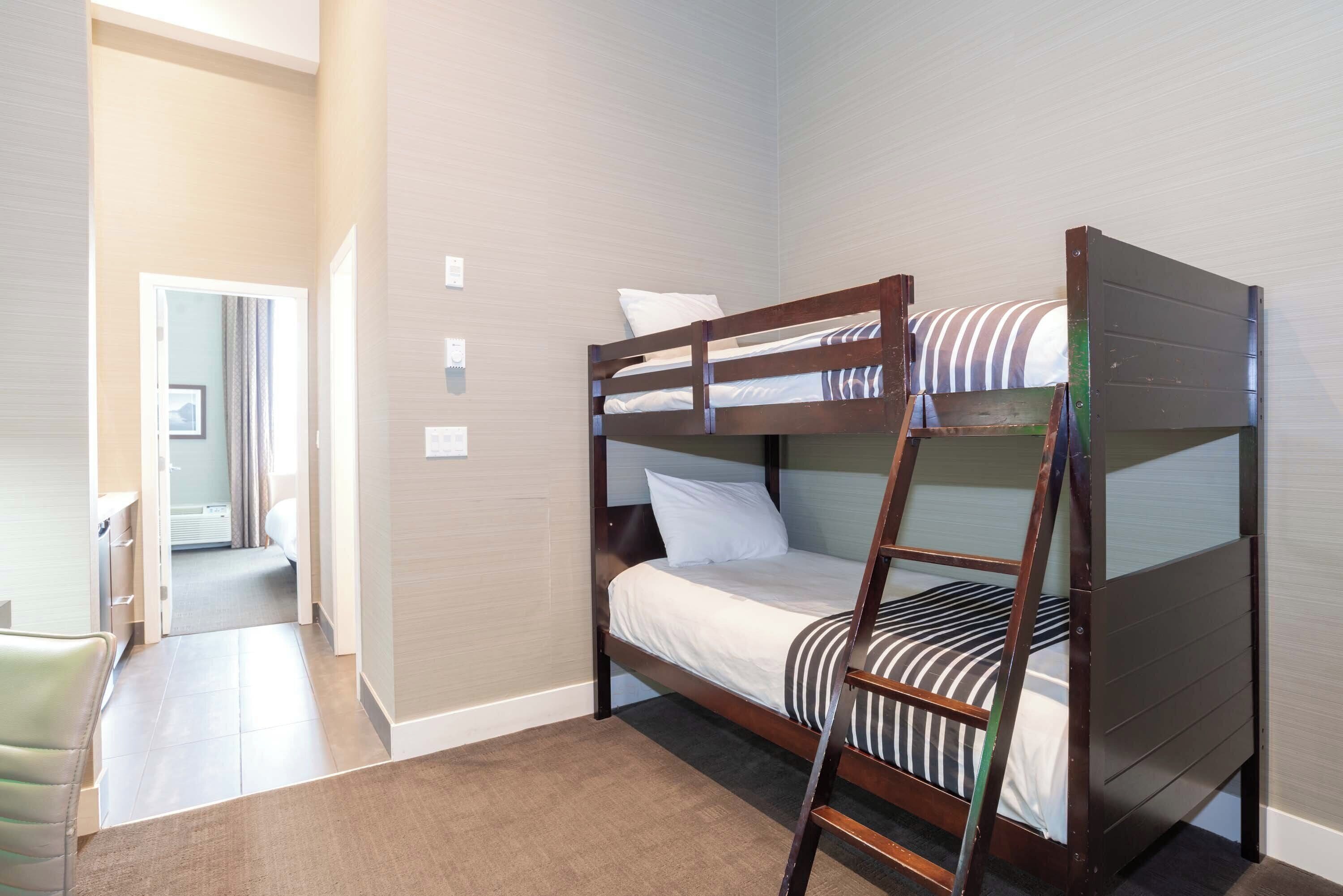 A bunk bed room with a wooden ladder, a small desk, and a chair.