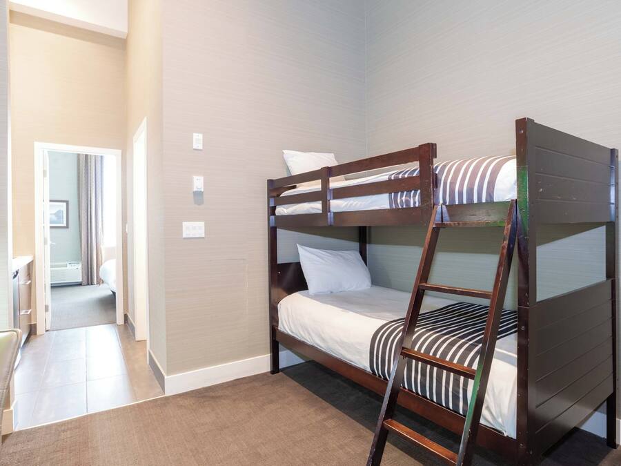 A bunk bed room with a wooden ladder, a small desk, and a chair.