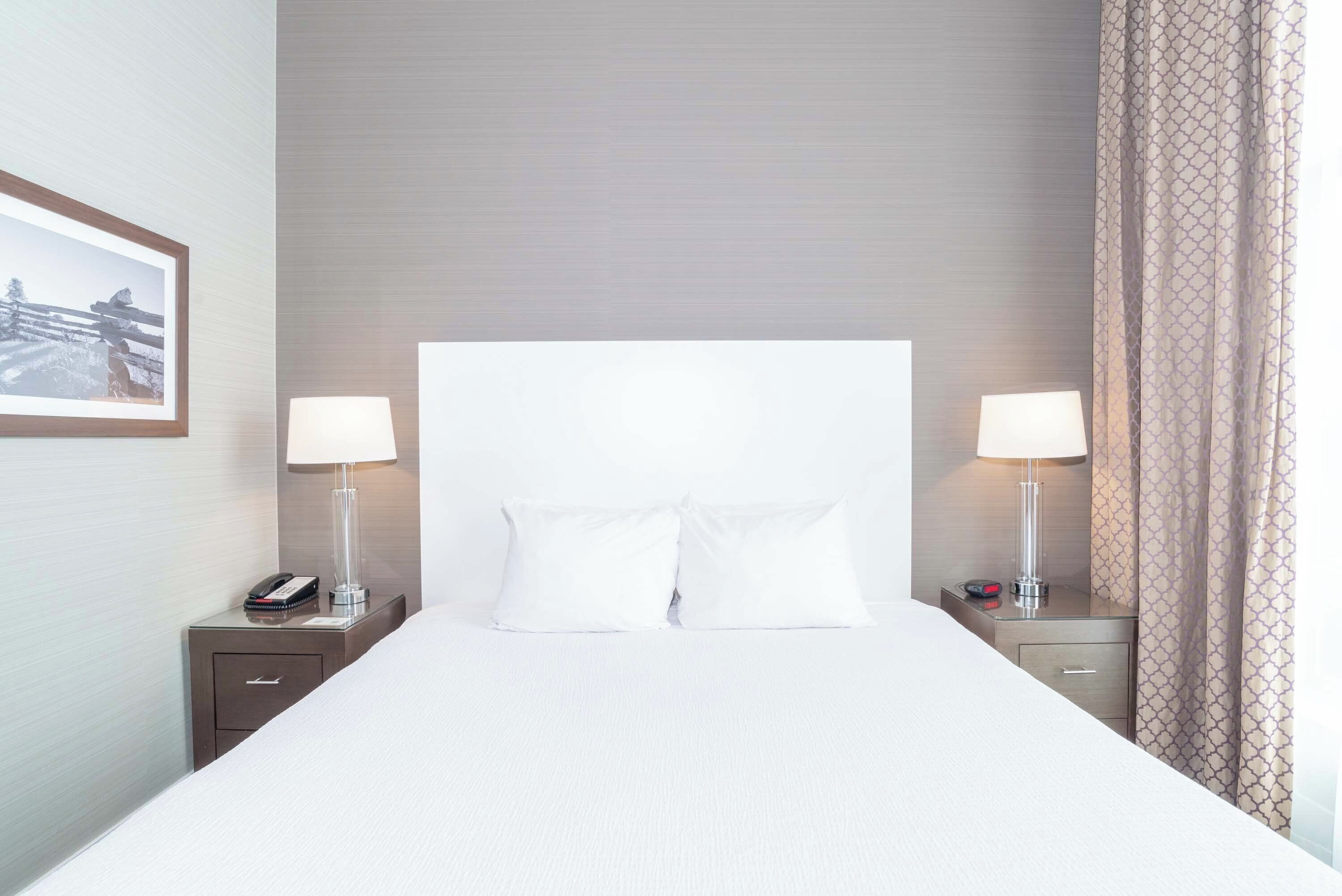 A hotel room with a large bed, two bedside tables, a nightstand, a framed picture on the wall, and a patterned curtain.