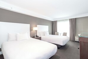 Een hotelkamer met twee bedden, een bureau, een stoel en een raam met gordijnen.