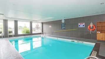 Una piscina interior con agua cristalina, marcas de profundidad y un flotador en la pared.