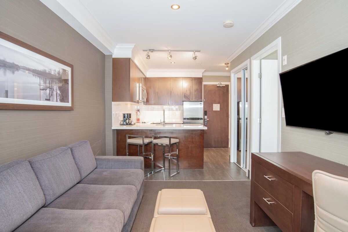 A modern living room with a gray sofa, a small ottoman, a wooden cabinet, and a flat-screen TV.