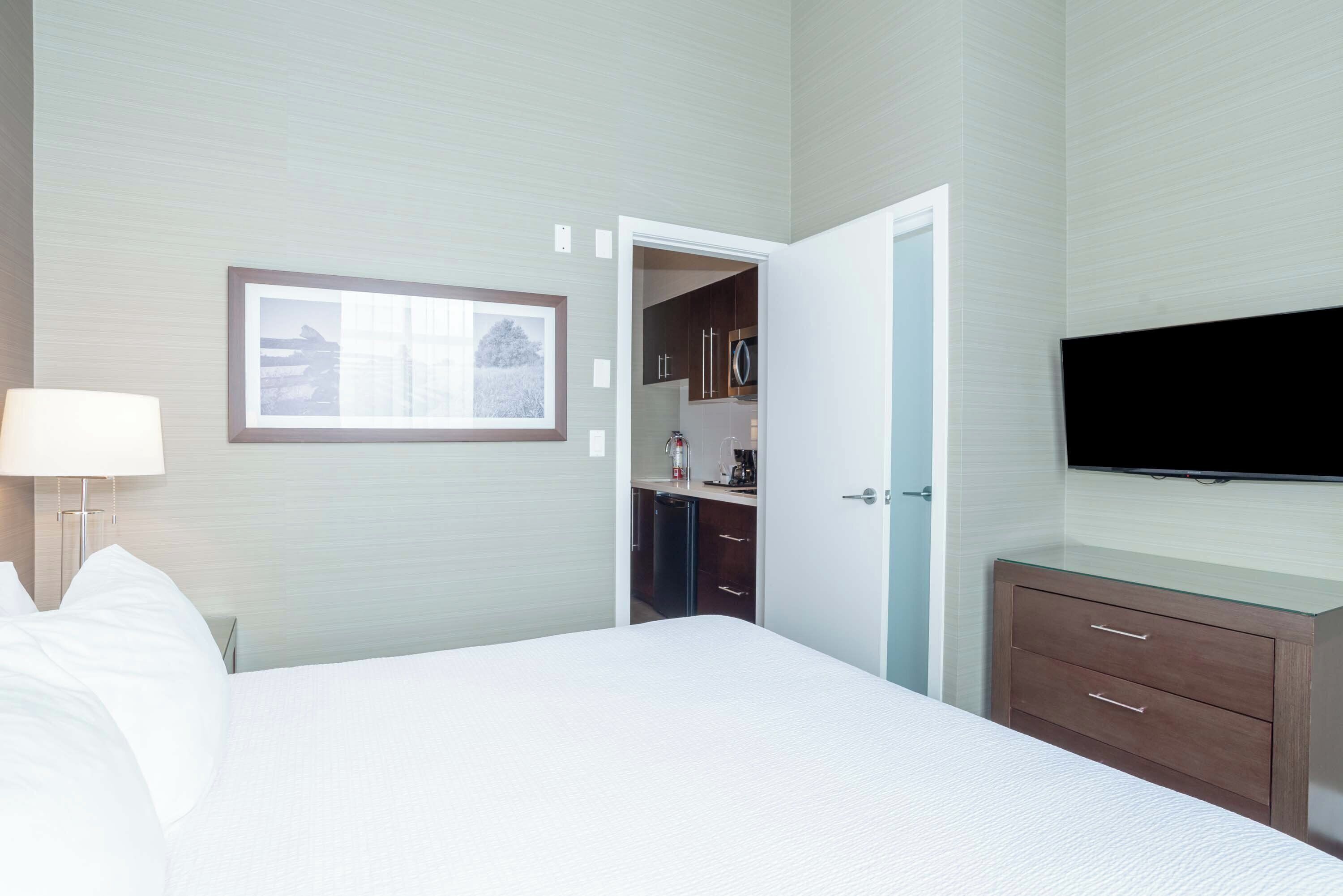 Een hotelkamer met een bed, een bedlamp, een televisie, een kledingkast en een kleine kitchenette.