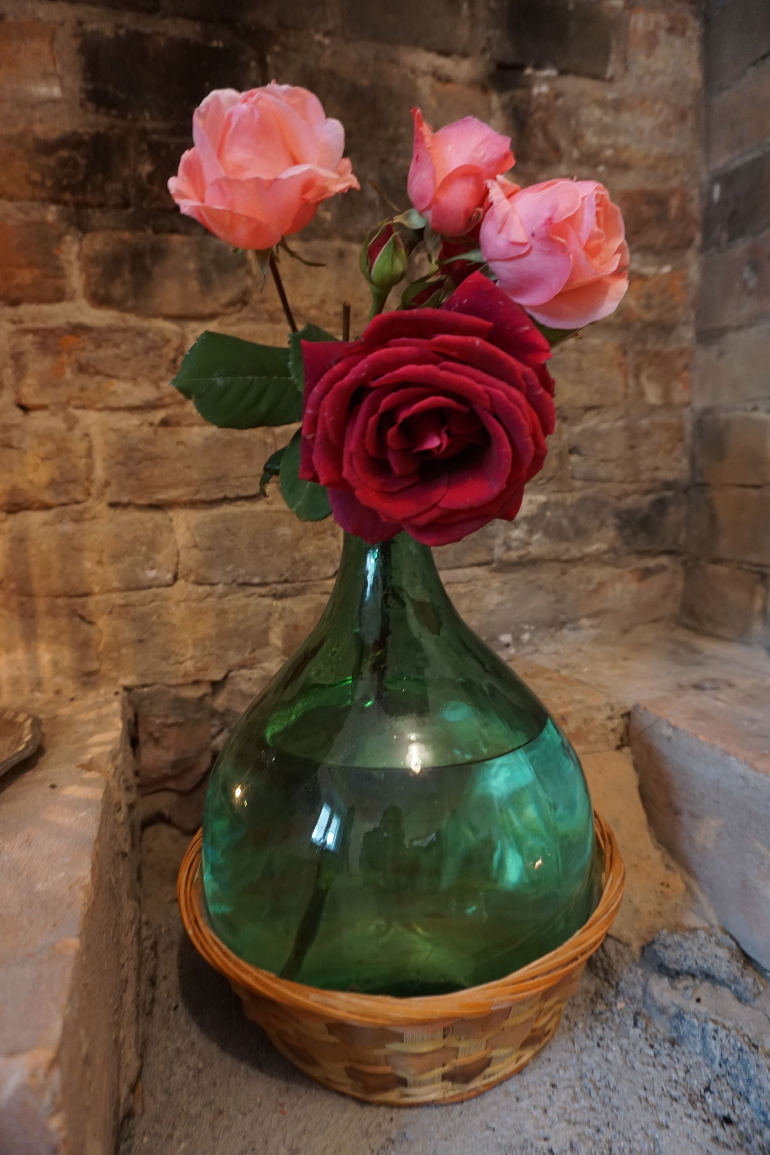 Eine grüne Glasvase mit gewebtem Sockel, gefüllt mit rosa und roten Rosen.
