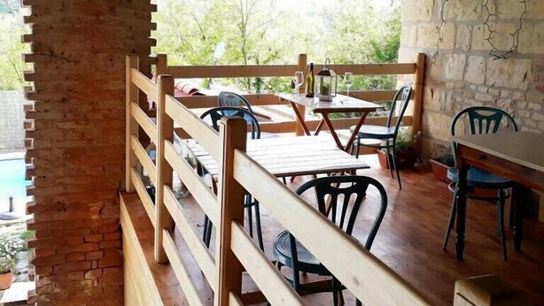 An outdoor dining area with wooden tables and chairs, a brick wall, and a view of greenery. - La Casa Blu Bed & Breakfast (Calliano)