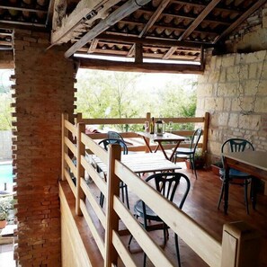 An outdoor dining area with wooden tables and chairs, a brick wall, and a view of greenery. - La Casa Blu Bed & Breakfast (Calliano)