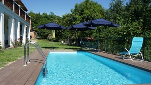 A swimming pool with a wooden deck, two umbrellas, and a blue lounge chair. - La Casa Blu Bed & Breakfast (Calliano)