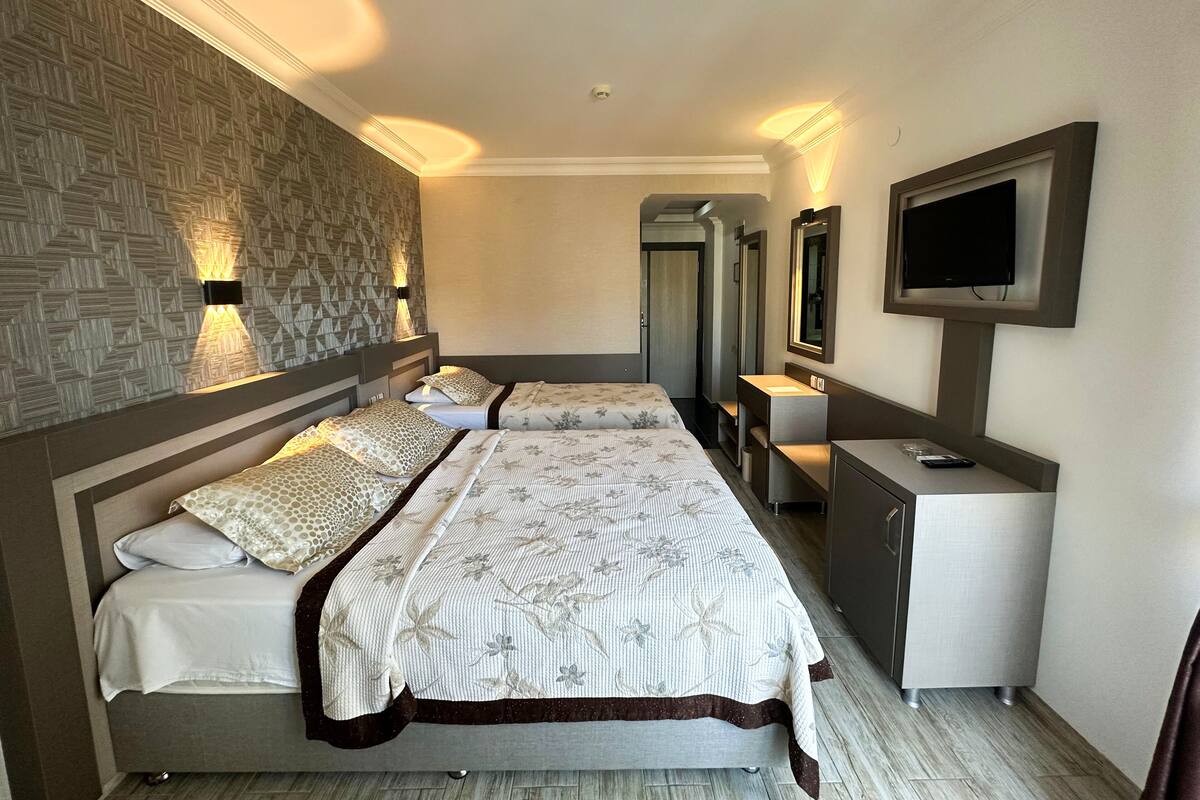 A hotel room with two beds, a TV, a mirror, and a vanity with a sink.