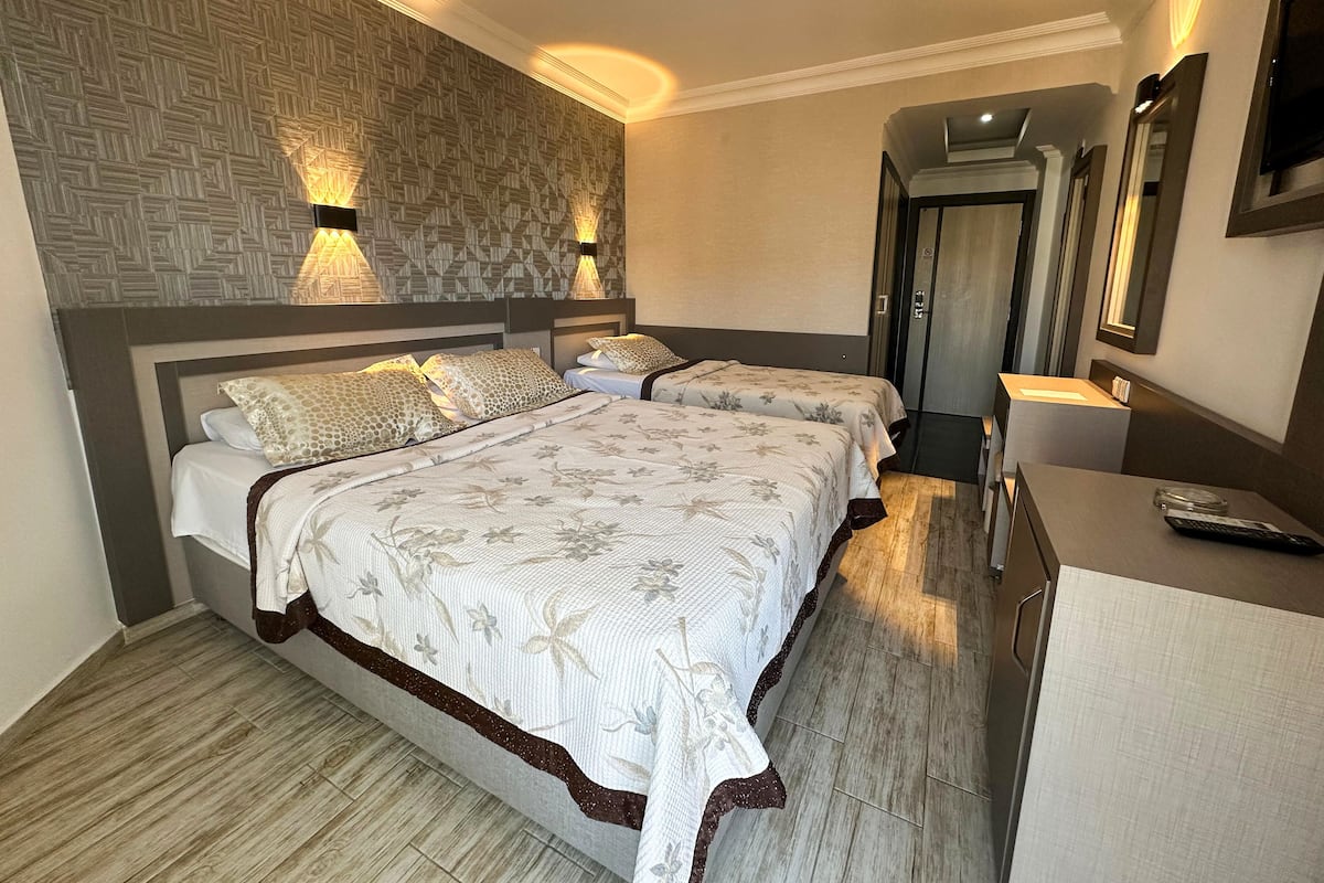 A hotel room with two beds, a wooden floor, a patterned wall, and a mirror.
