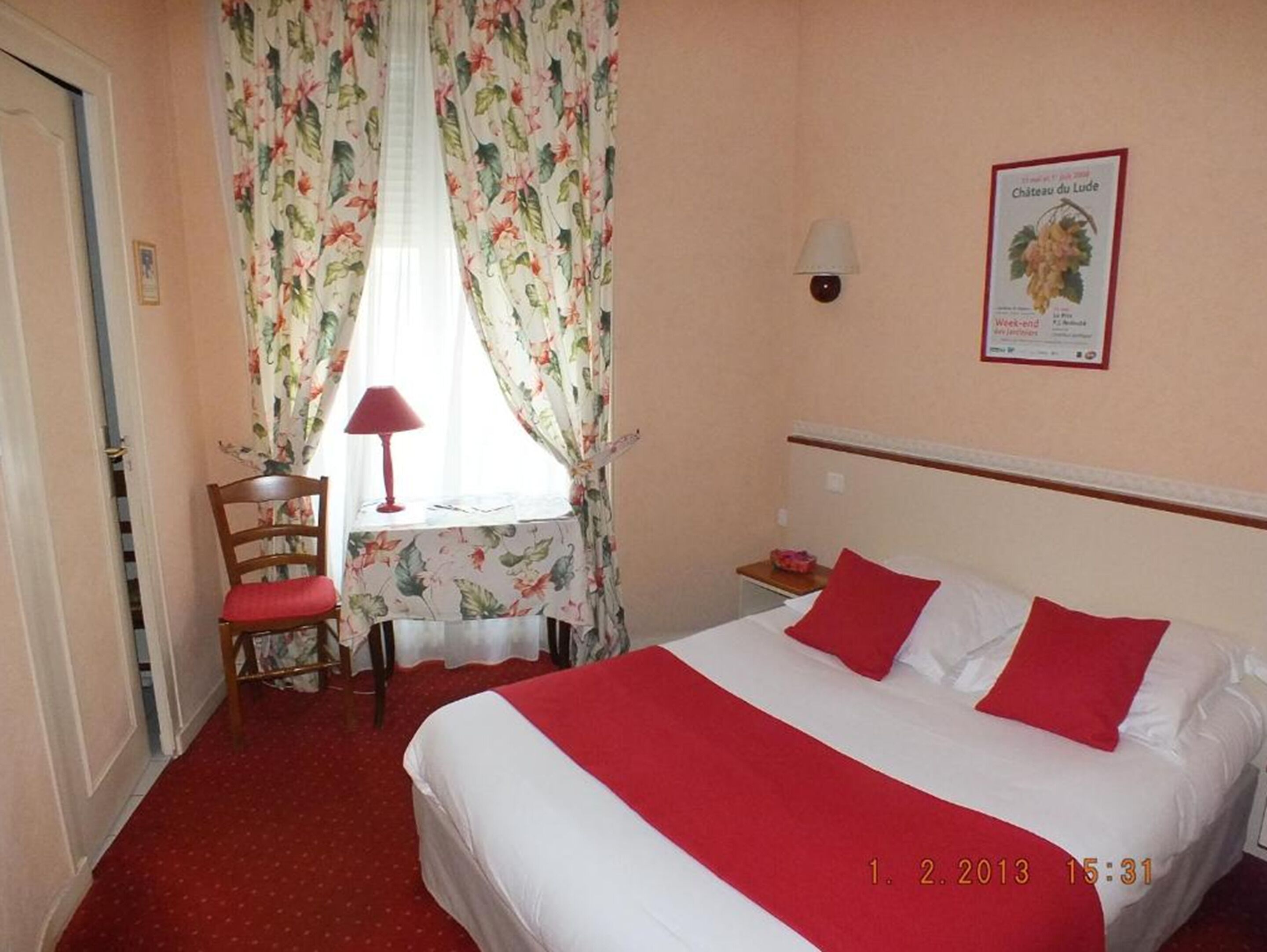 Een hotelkamer met een bed, een bureau met stoel, een lamp en een poster aan de muur.