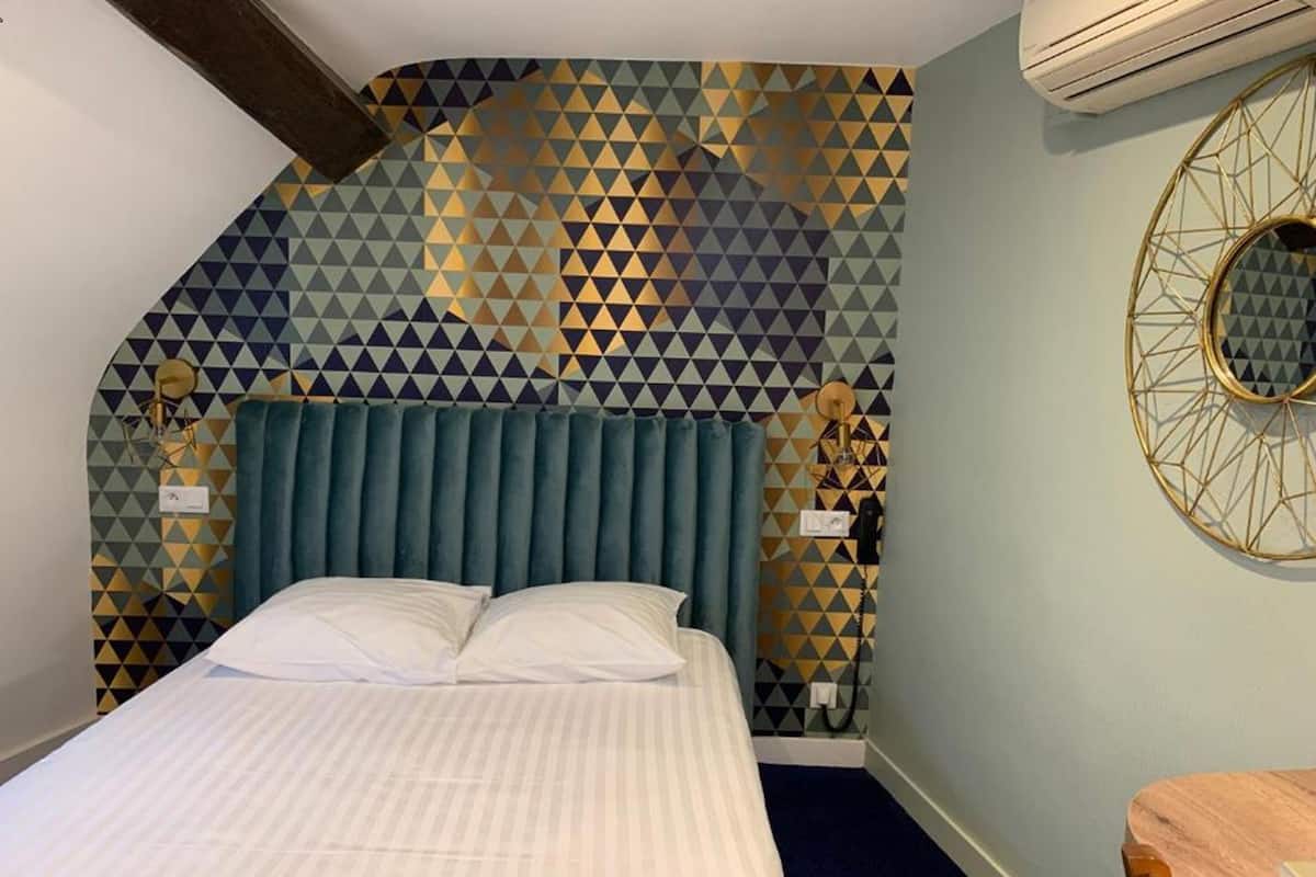 Una habitación con una cama, un papel tapiz de diseño geométrico, un espejo redondo y una silla de madera.