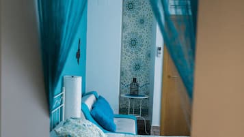 A bedroom with a bed, a bedside table, and a chair. There is a curtain partially drawn, revealing a bathroom with a toilet and a sink.