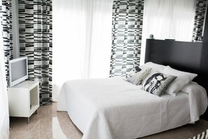 A modern bedroom with a large bed, a TV on a white stand, and black and white striped curtains. - Estudios Sierra de Francia  (Bejar)