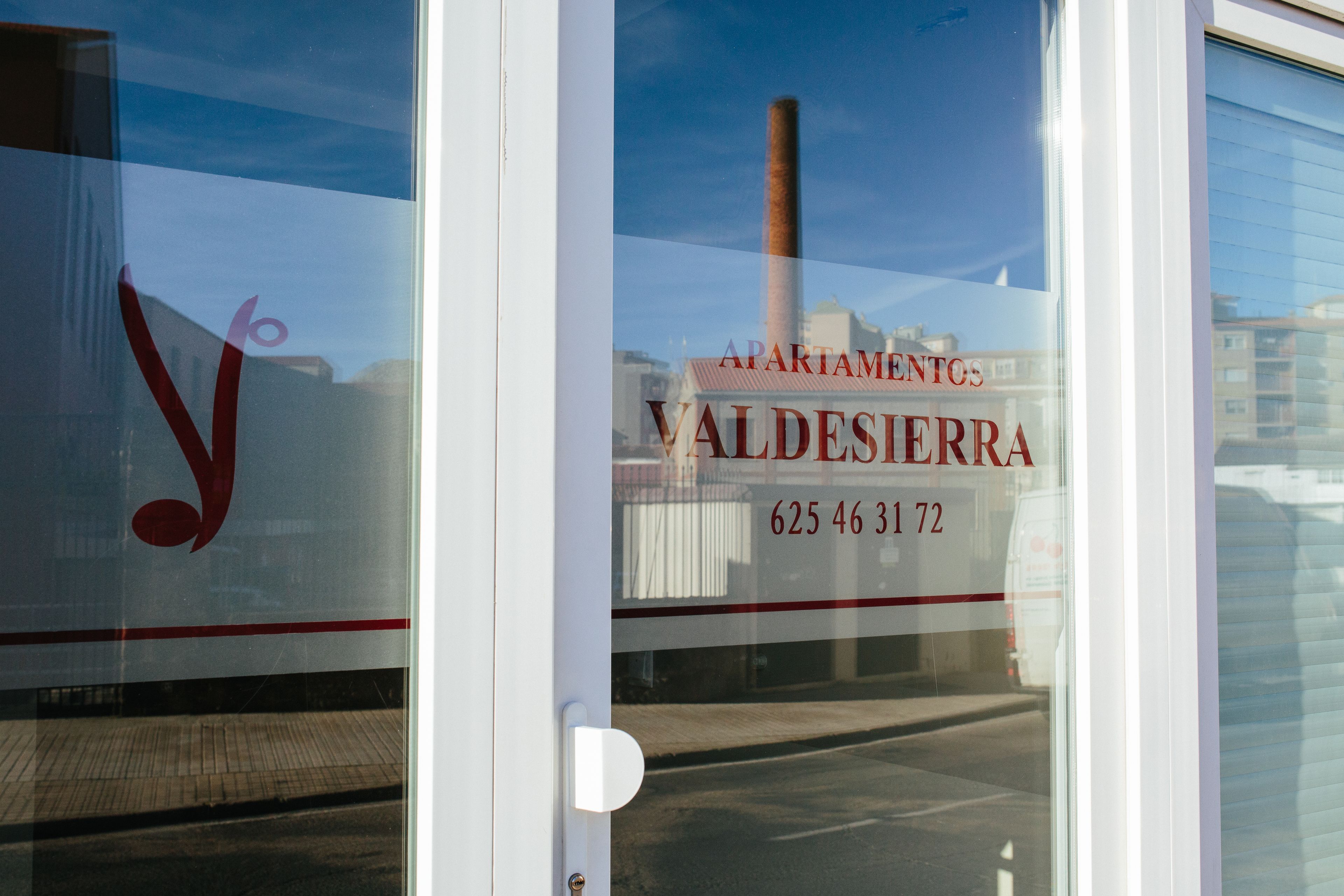 A window with a reflection of a building and a sign that reads "APARTAMENTOS VALDESIERRA 625 46 31 72".