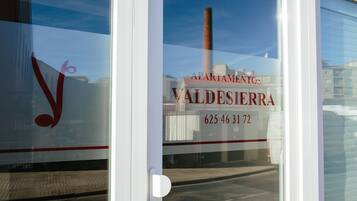A window with a reflection of a building and a sign that reads "APARTAMENTOS VALDESIERRA 625 46 31 72".
