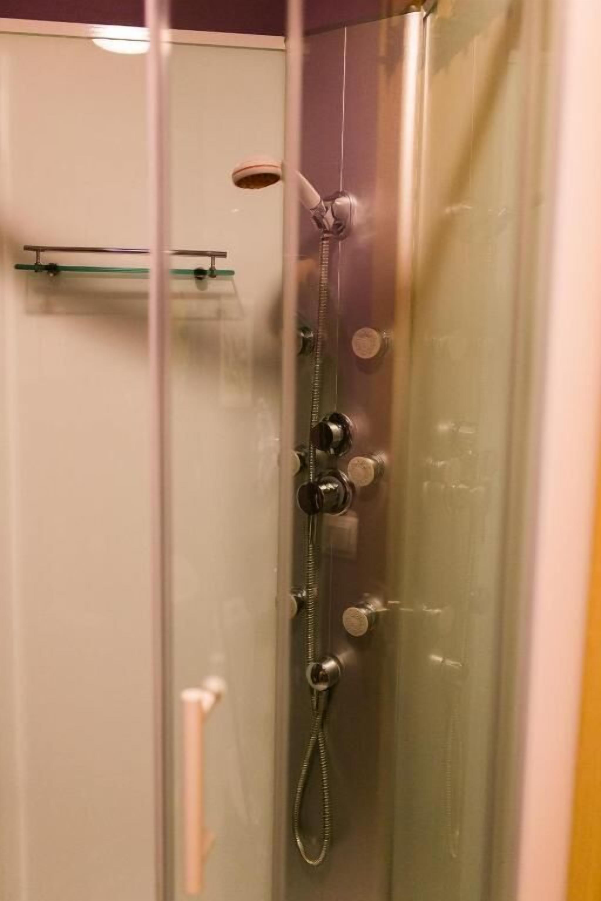 A glass-enclosed shower stall with a handheld showerhead, a wall-mounted faucet, and a control knob.