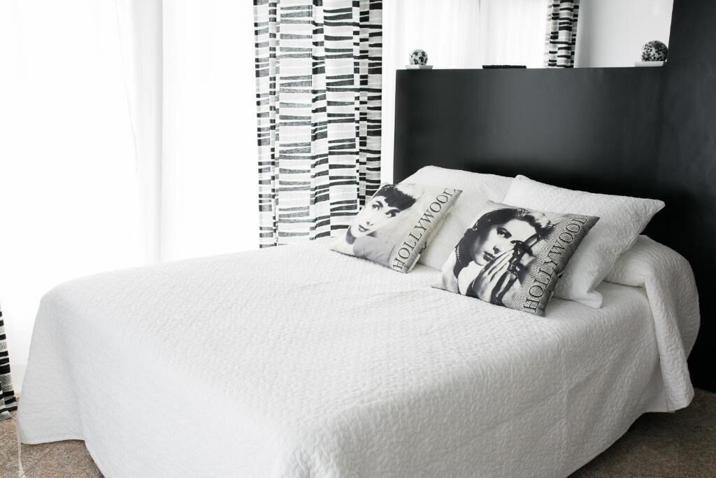 Una cama bien hecha con ropa de cama y almohadas blancas que tienen el texto 'Hollywood'.