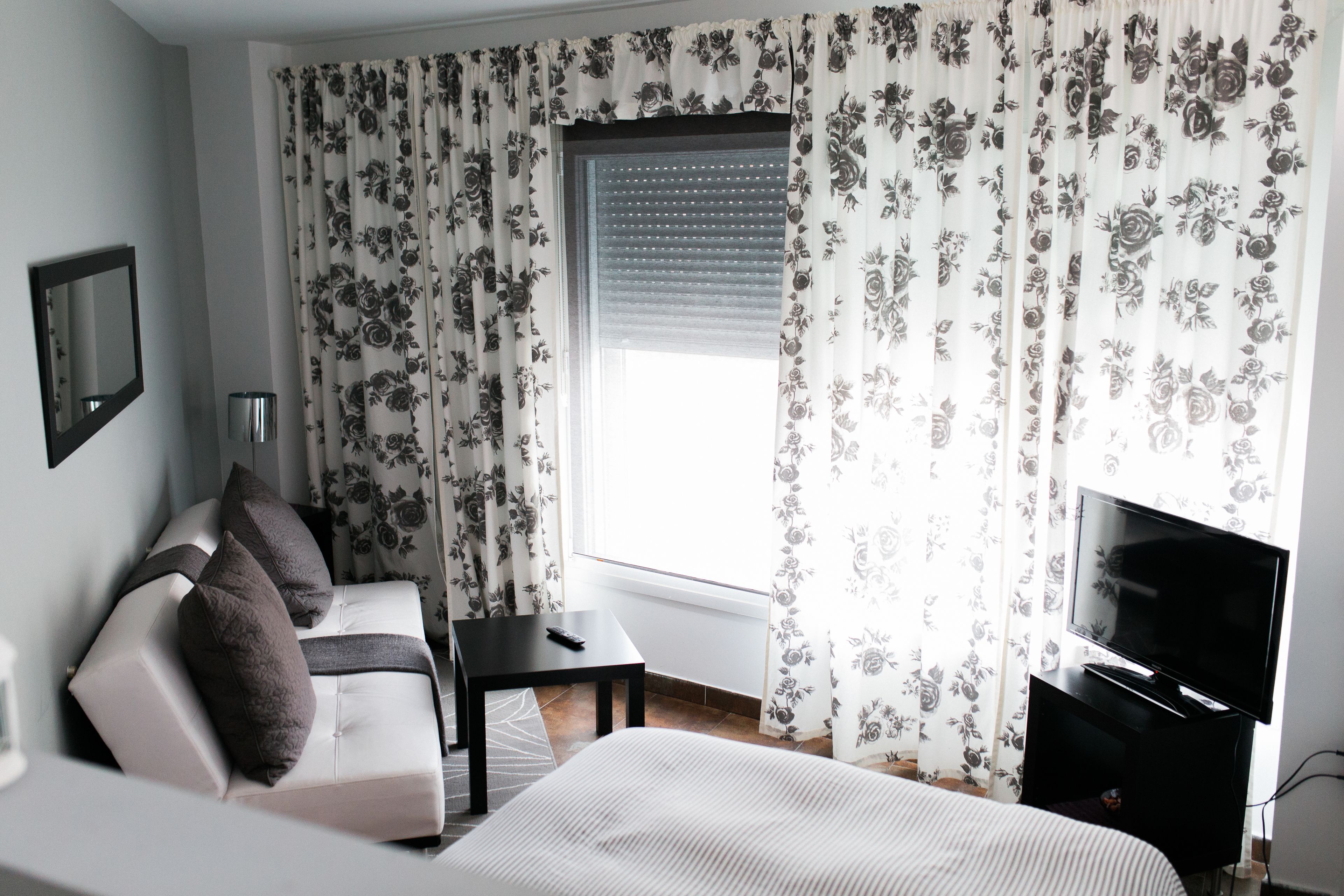 Une chambre d’hôtel avec un lit, un canapé, une télévision, une fenêtre avec des rideaux et un miroir.