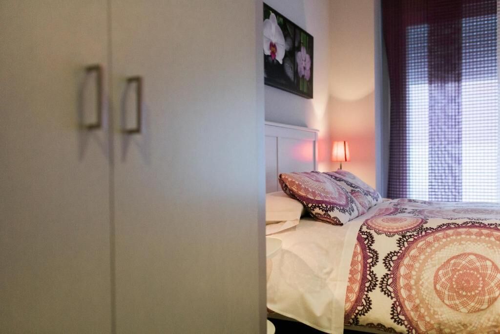 Ein Schlafzimmer mit einem Bett, einem Nachttisch, einer Wandlampe und einem Fenster mit Vorhängen.