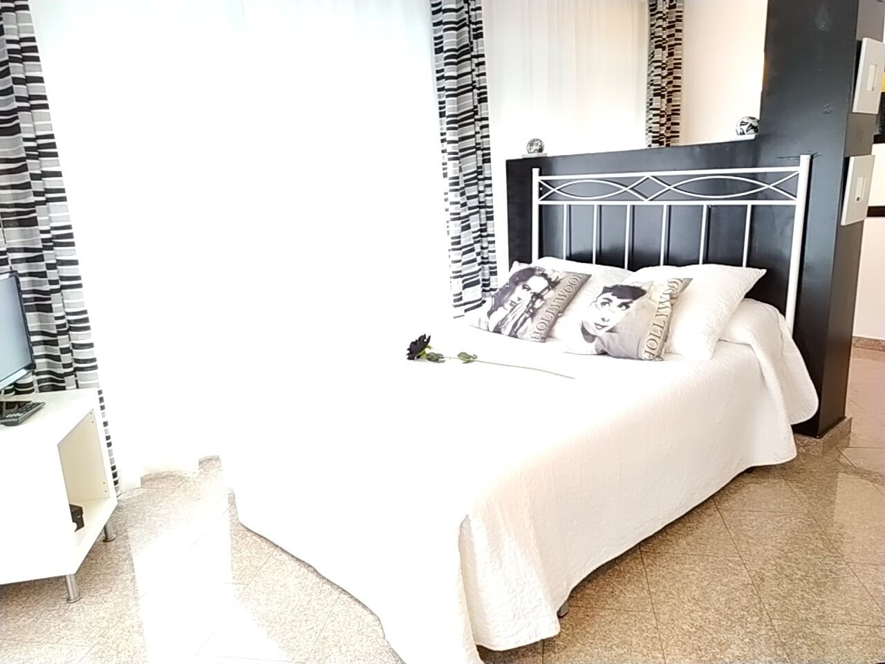 A neatly made bed with white bedding and decorative pillows, a modern headboard, and a small bedside table with a lamp.