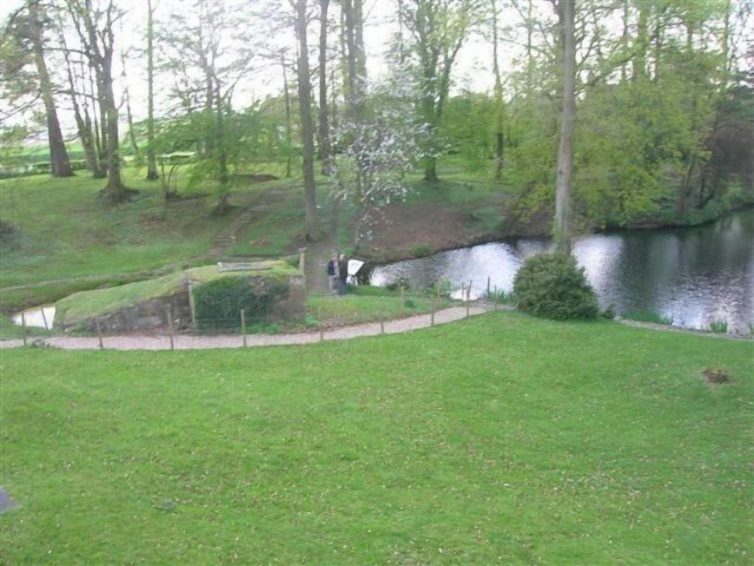 Un parque con un estanque, zonas verdes y árboles.