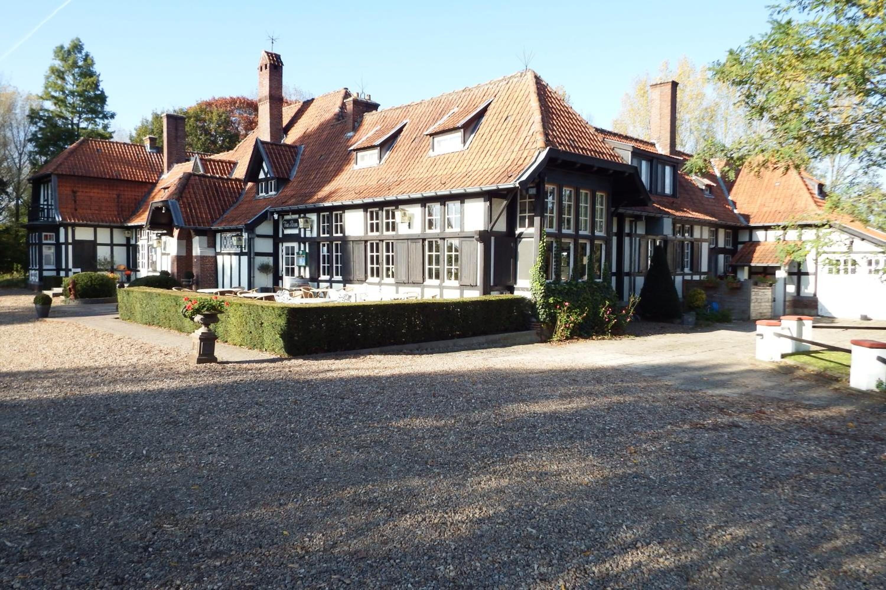 A traditional half-timbered building with a gravel driveway and a neatly trimmed hedge.