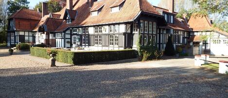 A traditional half-timbered building with a gravel driveway and a neatly trimmed hedge.