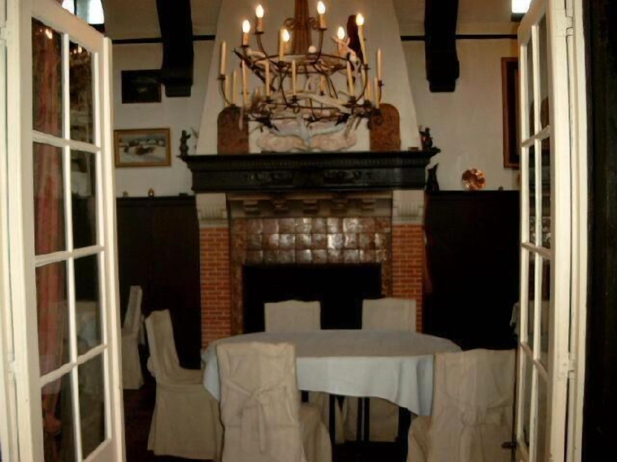 A dining area with a brick fireplace, a chandelier, and a table set for four.