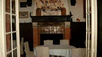 A dining area with a brick fireplace, a chandelier, and a table set for four.