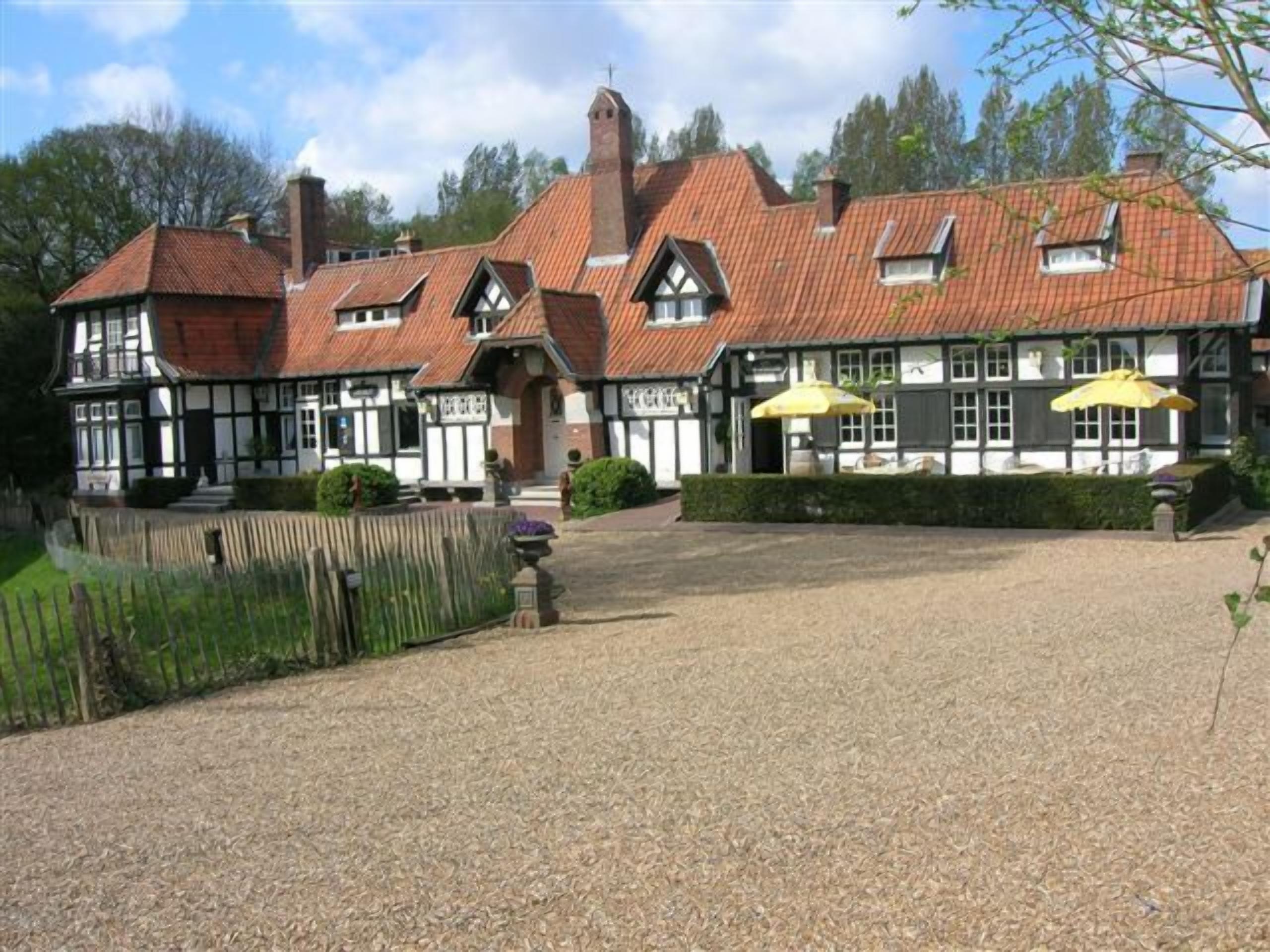 Un bâtiment traditionnel doté d’une cour en gravier, de nombreuses cheminées et d’une grande entrée.