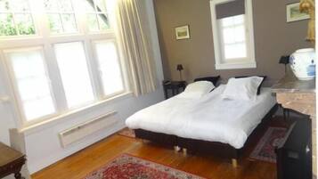 A bedroom with a bed, a window with curtains, a radiator, a nightstand, and a bedside table.