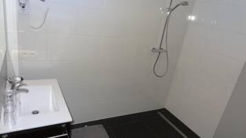 Une salle de bain avec un lavabo blanc, un miroir, une douchette à main et une douche avec un flexible.