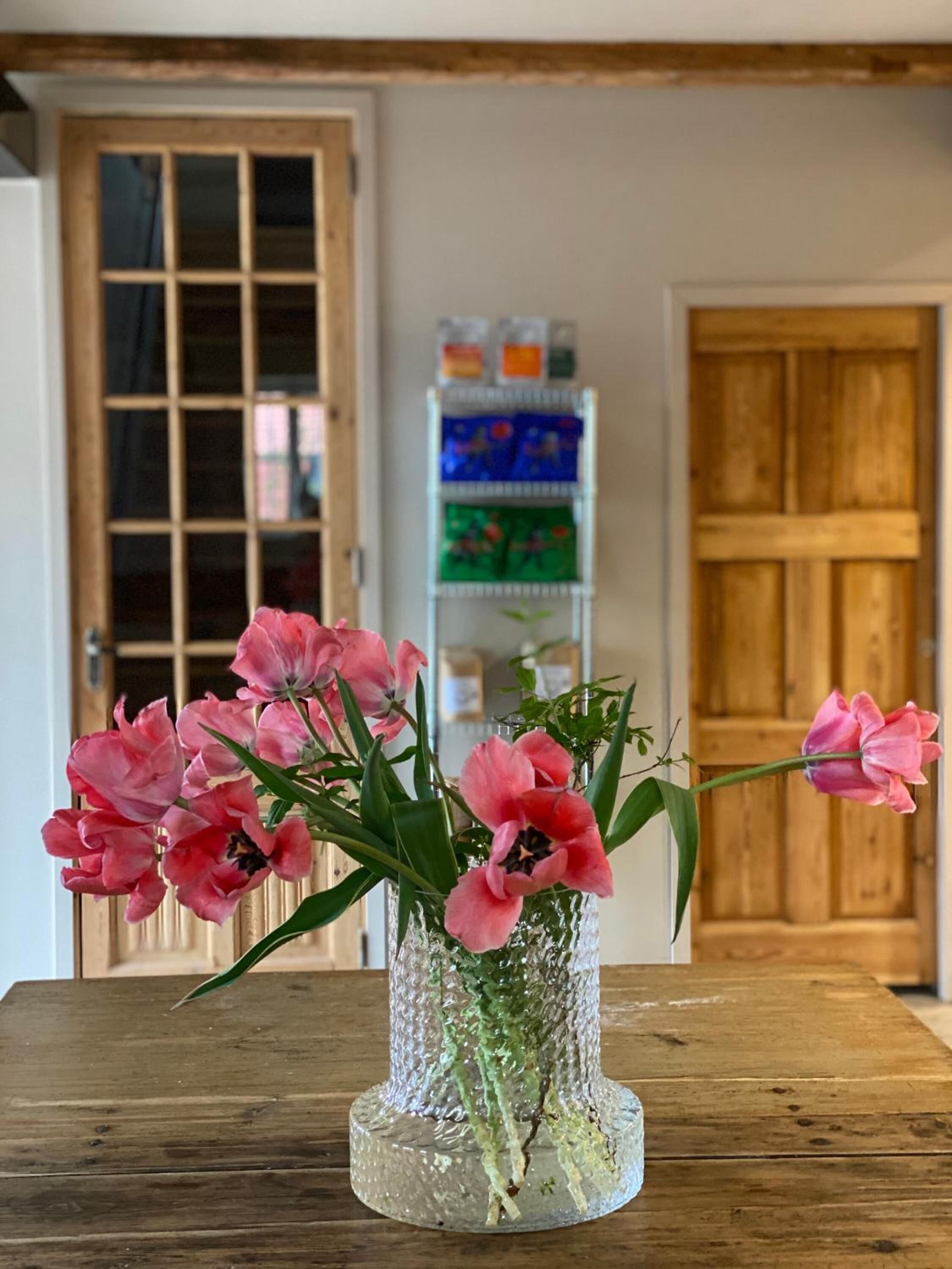 Un tavolo in legno con un vaso di vetro trasparente e fiori rosa.