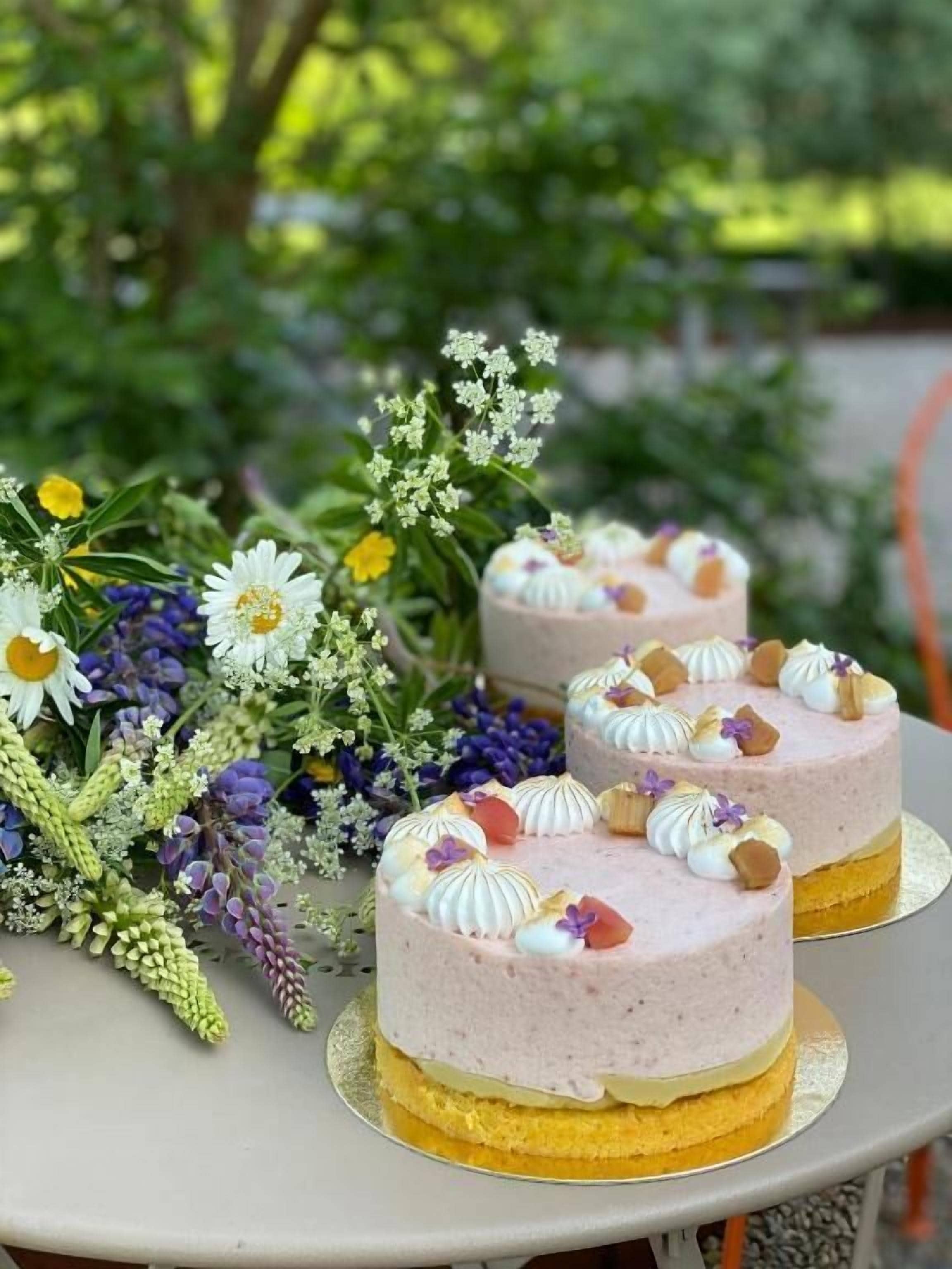 Dos pasteles redondos con decoración encima, sobre una mesa, rodeados de diversas flores.
