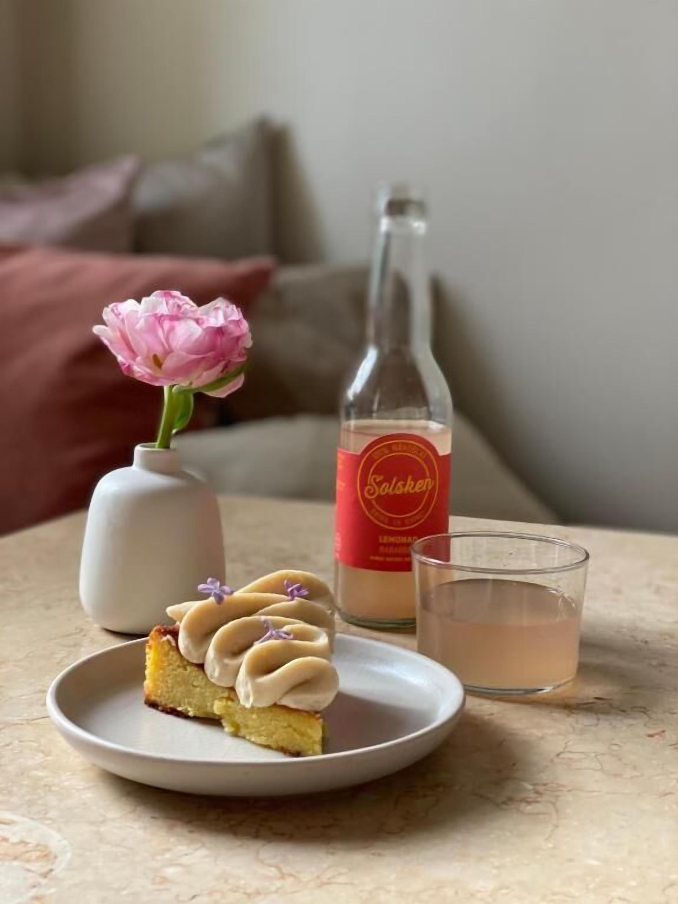 A slice of cake on a plate, a bottle of Solisken, and a glass of liquid on a table.