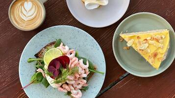 A wooden table with a candle, a cup of coffee, a plate with a dessert, a slice of pie, and a plate with shrimp and greens.