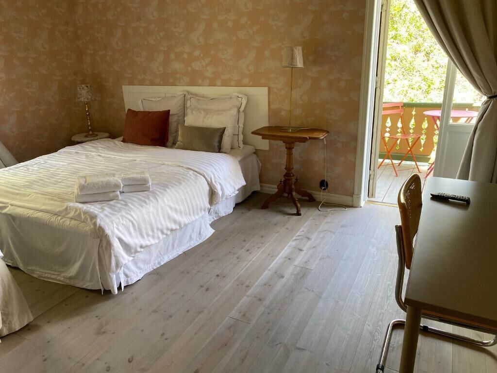 A hotel room with a bed, a small table, a chair, and a view of the outdoors.