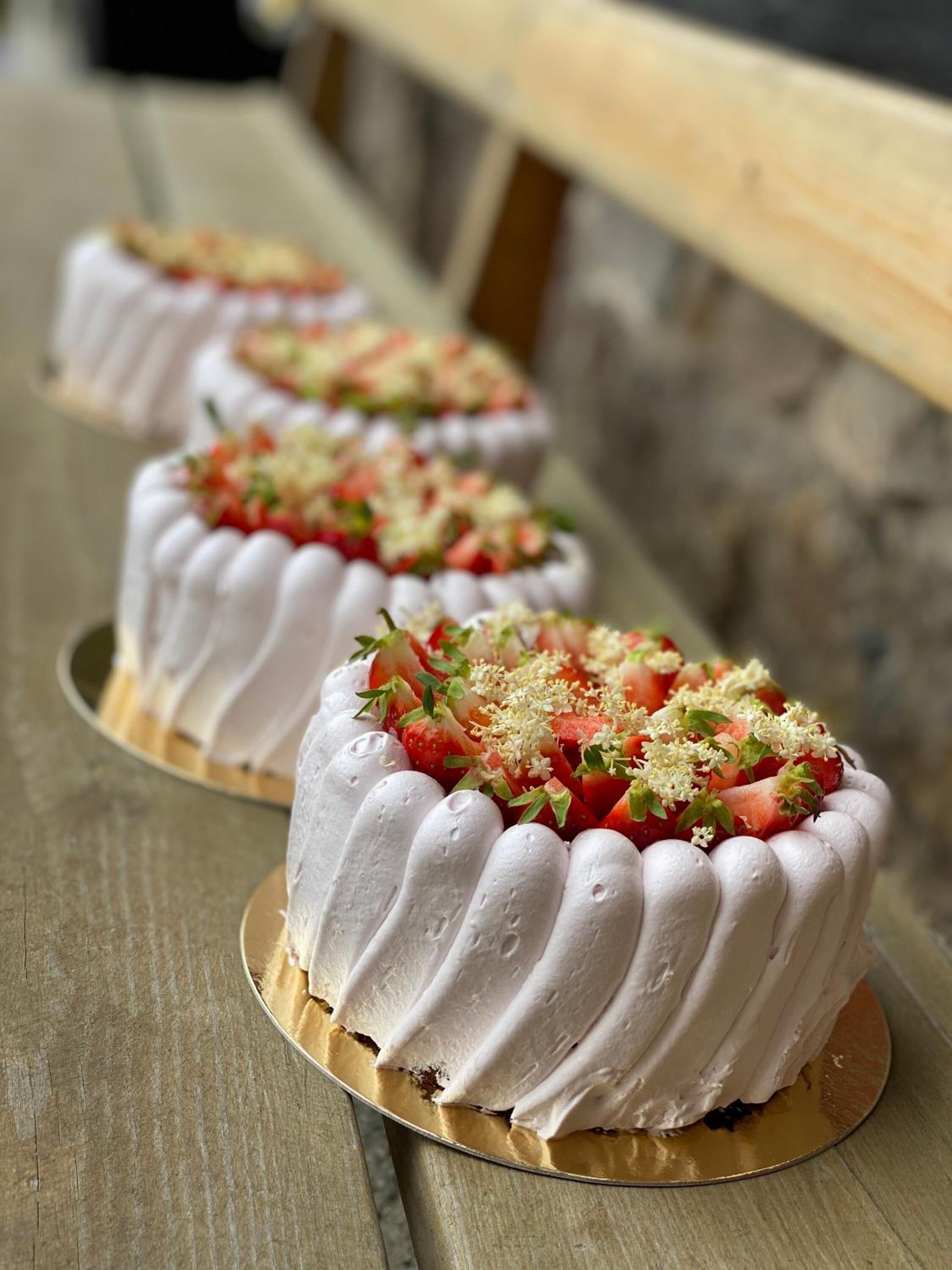 Three white frosted cakes with strawberries and green garnish on a wooden table.