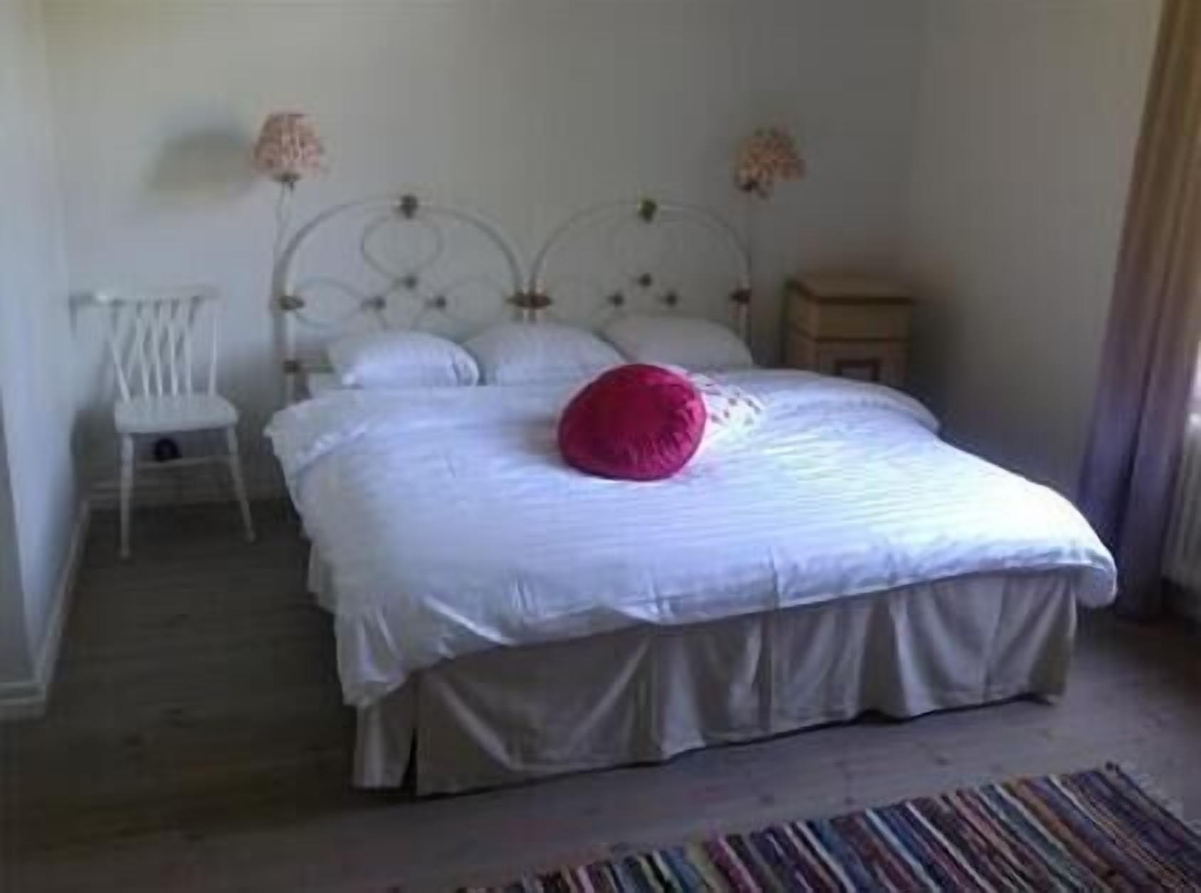Un dormitorio con cama, una silla, una mesita de noche y una lámpara.