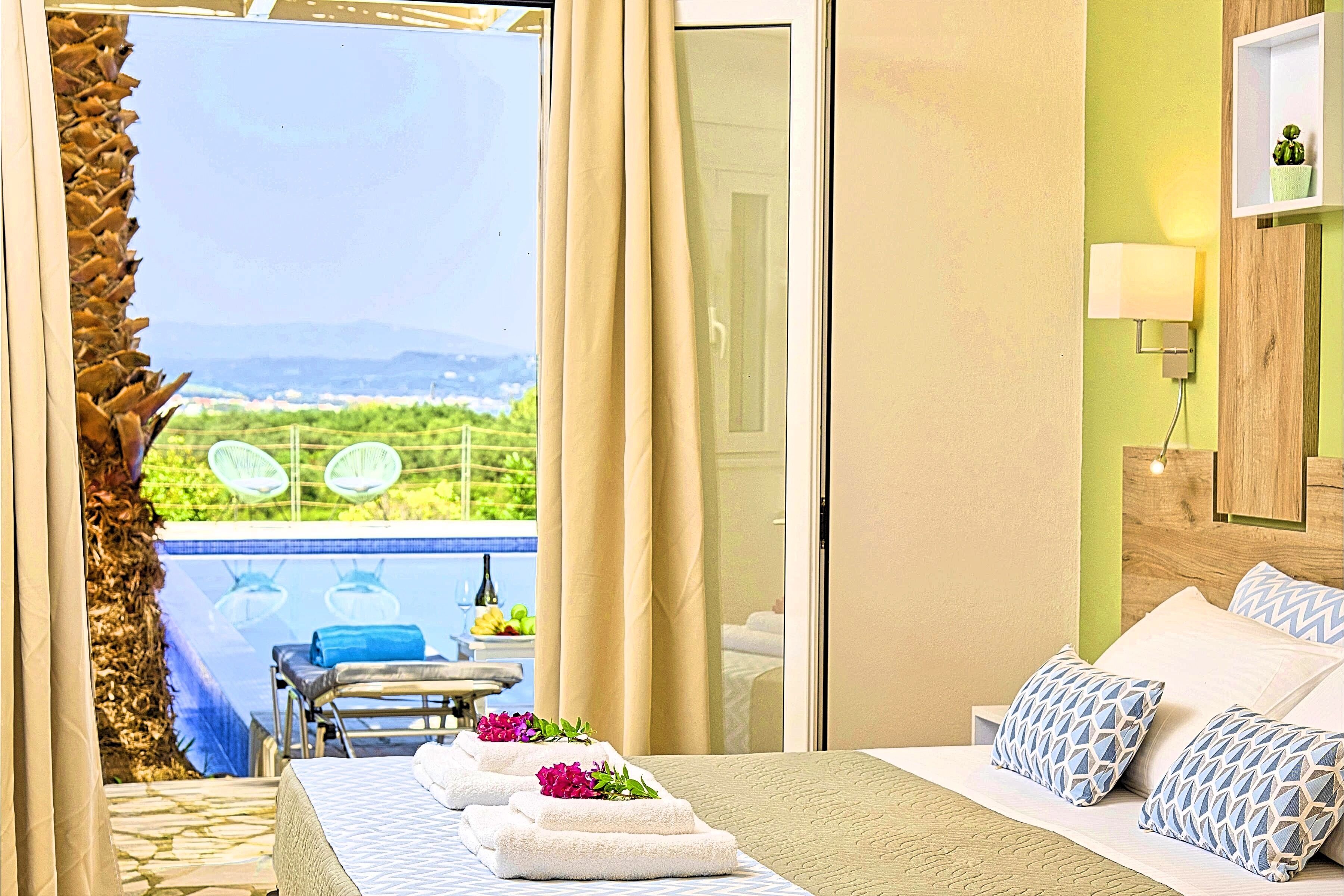 A hotel room with a bed, a view of a pool, and a dining area with chairs and a table.