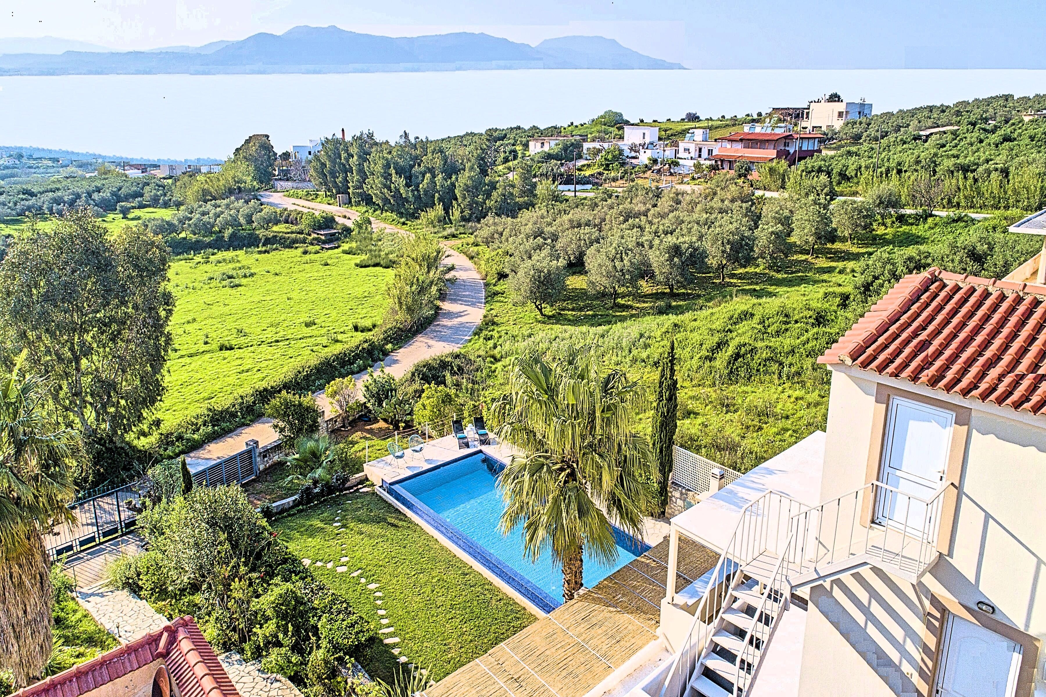 A residential area with a swimming pool, lush greenery, and a view of the sea.