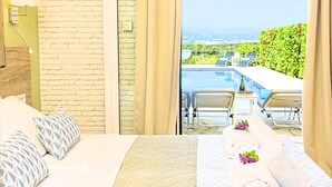 A hotel room with a bed, a view of a pool and outdoor seating, and a brick wall. - Cretan Mansion with Heated Swimming Pool (Apokoronas)