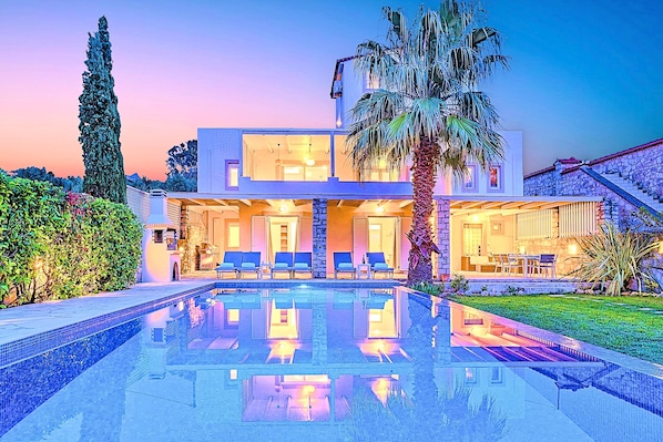 A modern two-story house with a swimming pool, outdoor seating, and a staircase leading to a stone roof.